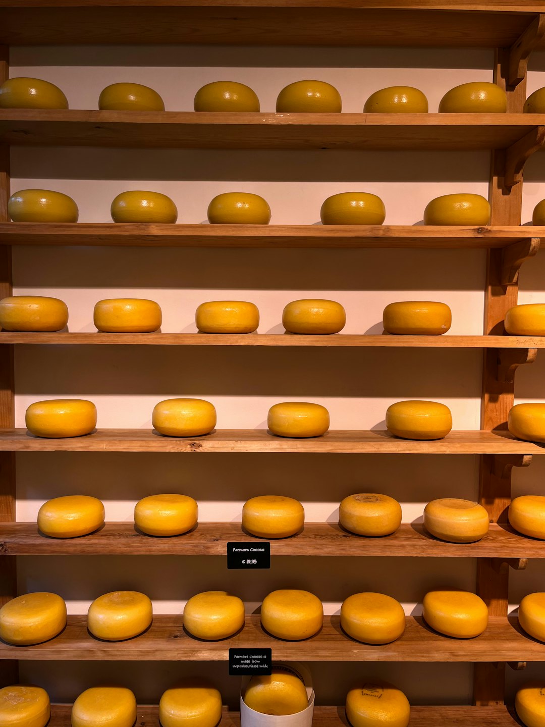 Ruedas de queso amarillo redondas apiladas en estantes de madera.